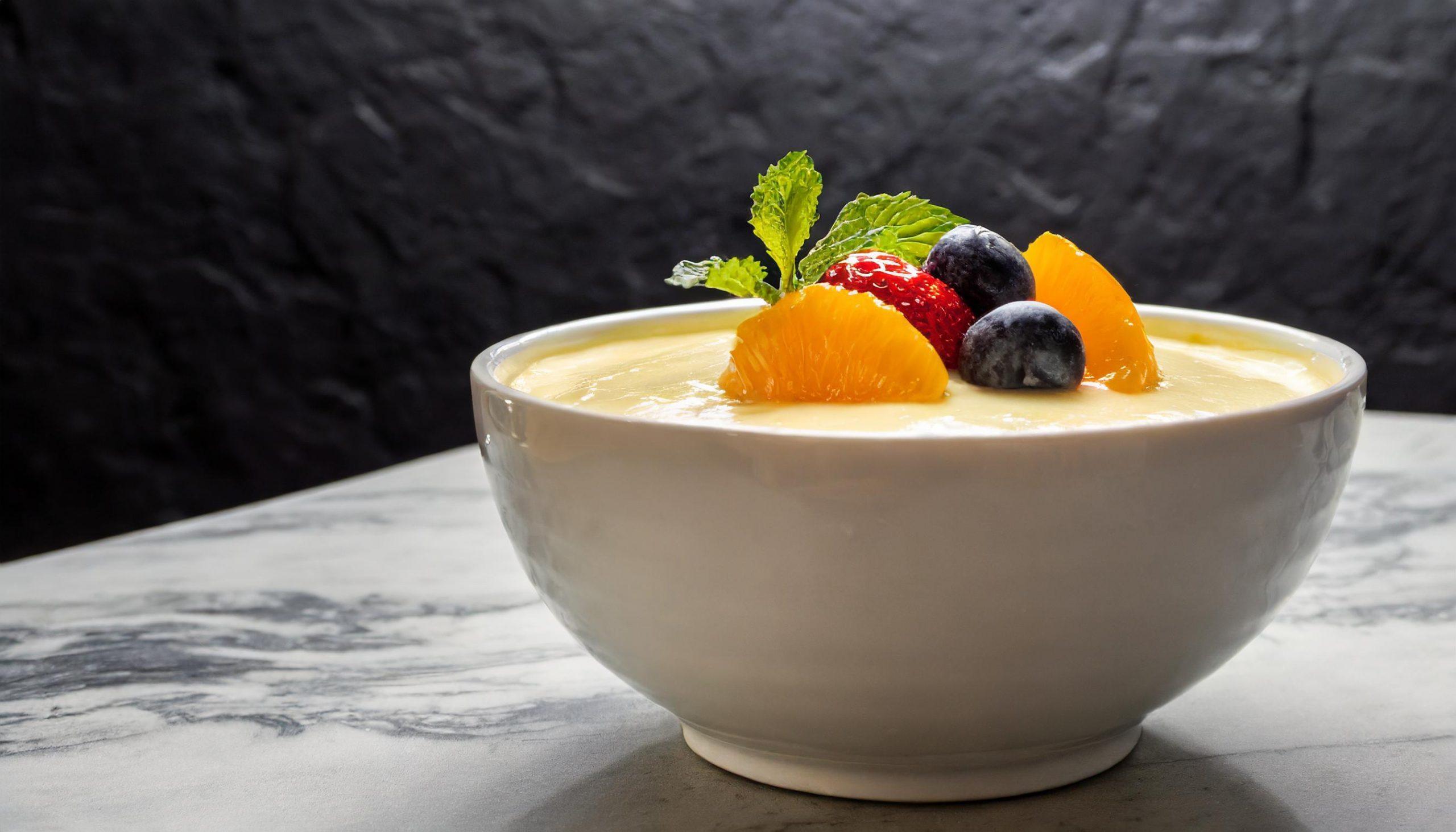 Nahaufnahme eines rustikalen weißen Granittischs vor einem schwarzen, strukturierten Schieferhintergrund, auf dem ein Glas Vanillepudding dekorativ arrangiert ist.