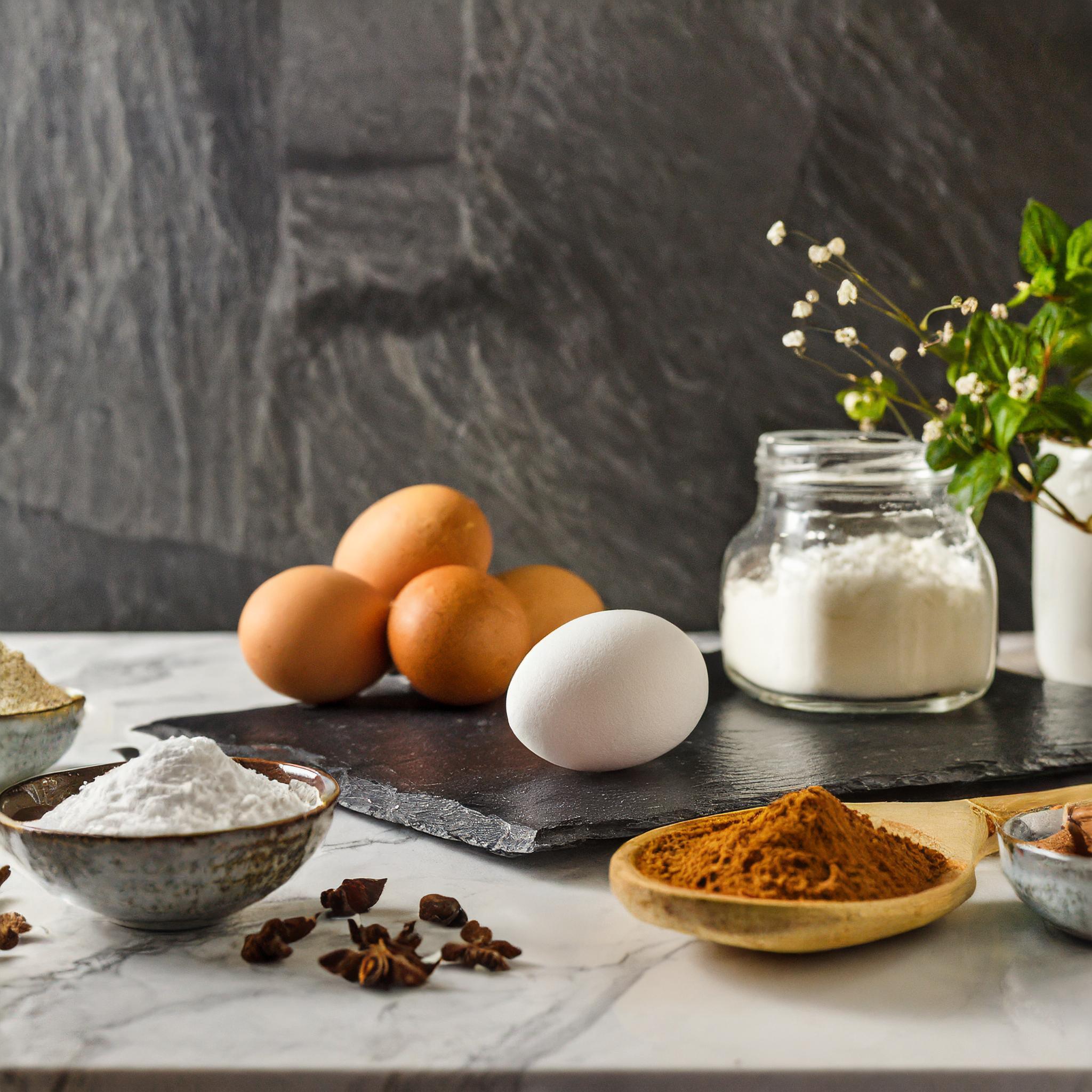 Nahaufnahme eines rustikalen weißen Granittischs vor einem schwarzen, strukturierten Schieferhintergrund, auf dem ein frisch gebackener Biskuitboden dekorativ arrangiert ist.