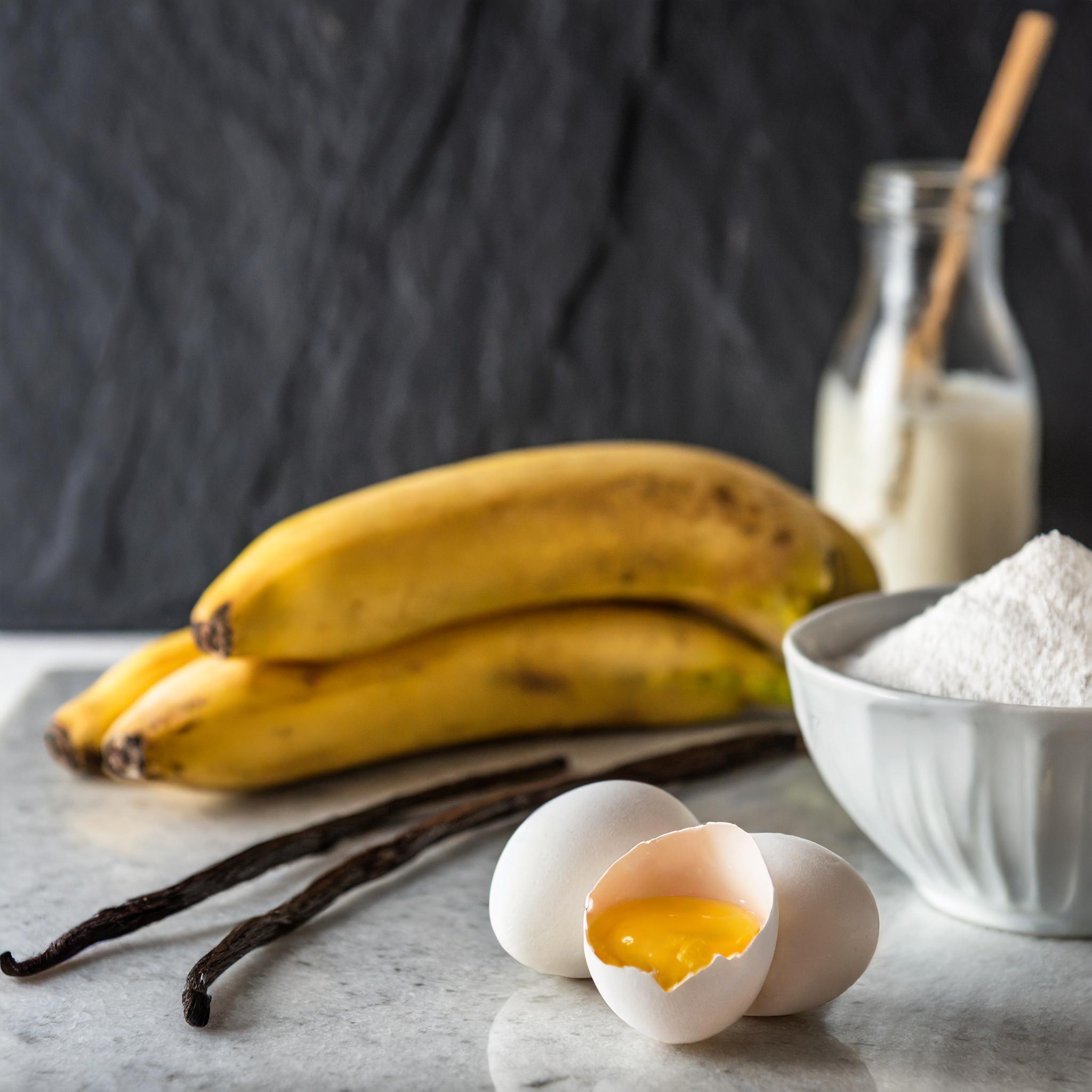 Nahaufnahme eines rustikalen weißen Granittischs vor einem schwarzen, strukturierten Schieferhintergrund, auf dem ein frisch gebackenes Bananenbrot dekorativ arrangiert ist.